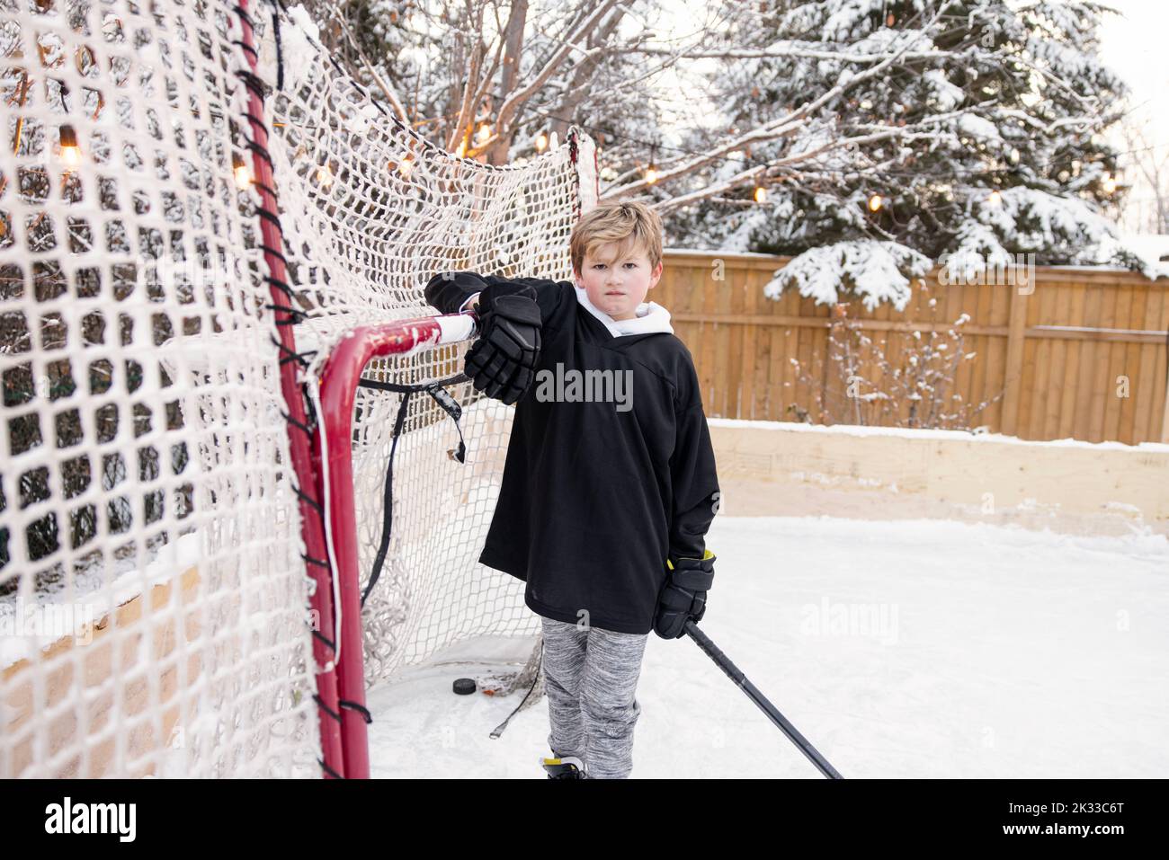 Portrait selbstbewusster Junge im Eishockey-Netz auf verschneite Hinterhof-Eisbahn Stockfoto