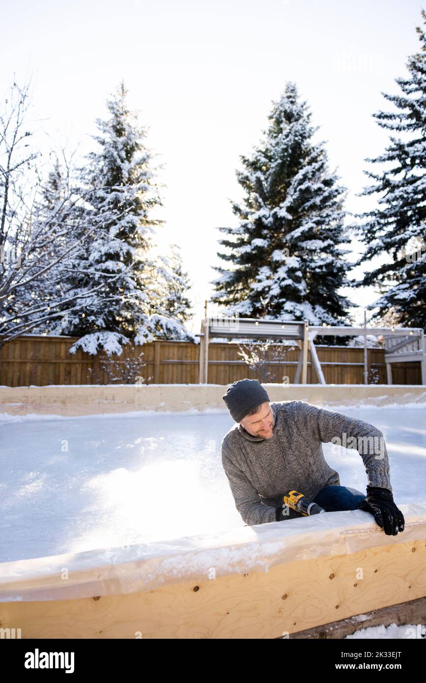 Mann mit Bohrmaschine beim Bau einer Eisbahn im verschneiten Hinterhof Stockfoto
