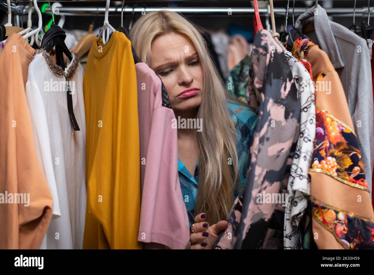 Eine traurige blonde Frau, die in einem Bekleidungsgeschäft einkauft. Stockfoto