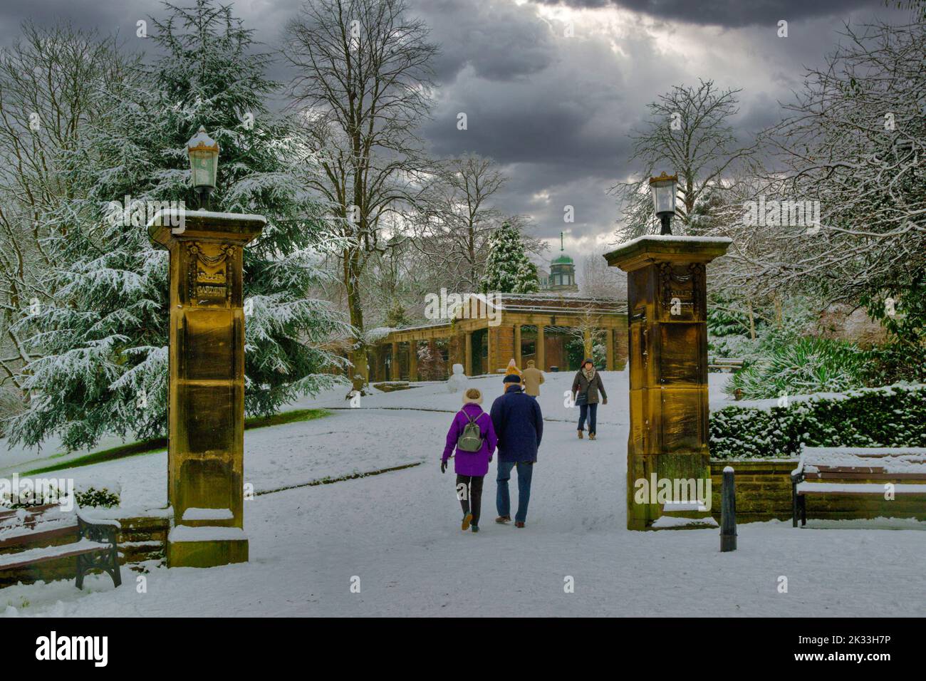 Touristen, die an einem kalten Dezembermorgen durch die Valley Gardens wandern, mit Schnee auf dem Boden und Bäumen, Harrogate, Yorkshire. VEREINIGTES KÖNIGREICH. Stockfoto