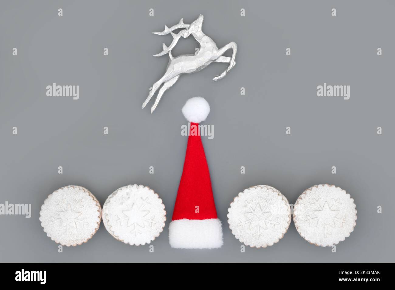 Weihnachtsfeiertage festliche Symbole mit weihnachtsmütze, Rentieren und Hackfleisch Kuchen auf grauem Hintergrund. Traditionelle Baumdekorationen und Essen abstrakt. Stockfoto