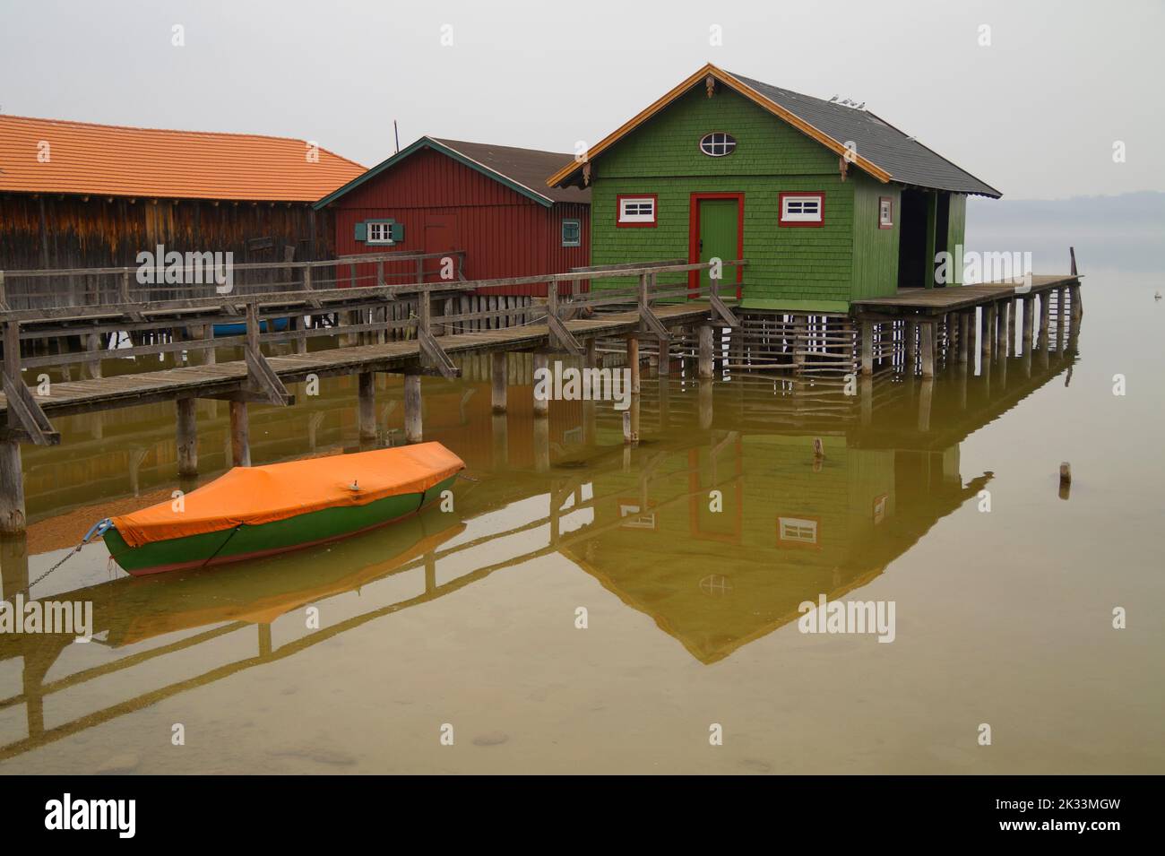 Lange hölzerne Seebrücke, die an trüben und nebligen Tagen zu den bunten Bootshäusern am Ammersee im bayrischen Dorf Schondorf führt (Bayern, Deutschland) Stockfoto