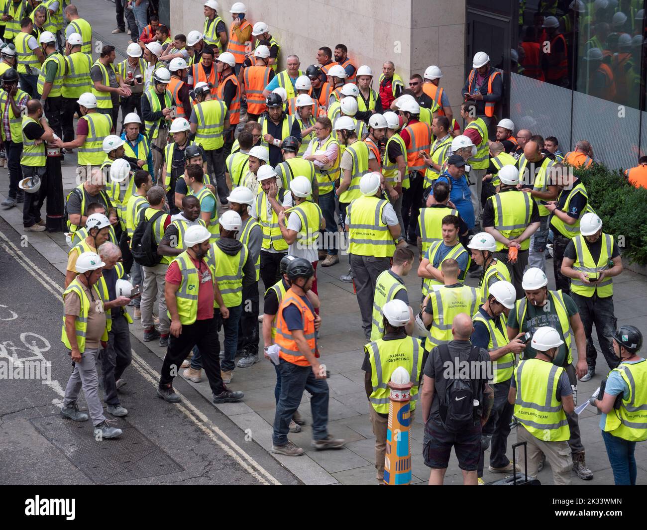 Massen von Bauarbeitern und Bauunternehmern, die Leuchtstoffjacken und Hüte tragen, versammeln sich während der Evakuierungsfeuerübung in Barbican London vor dem Gebäude Stockfoto