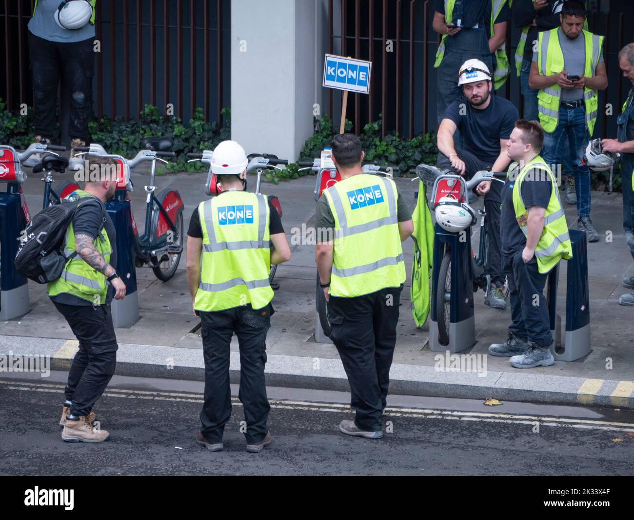 Massen von Bauarbeitern und Auftragnehmern, die Kone-Leuchtstoffjacken und -Hüte tragen, versammeln sich während der Evakuierungsfeuerübung in Barbican London vor dem Gebäude Stockfoto