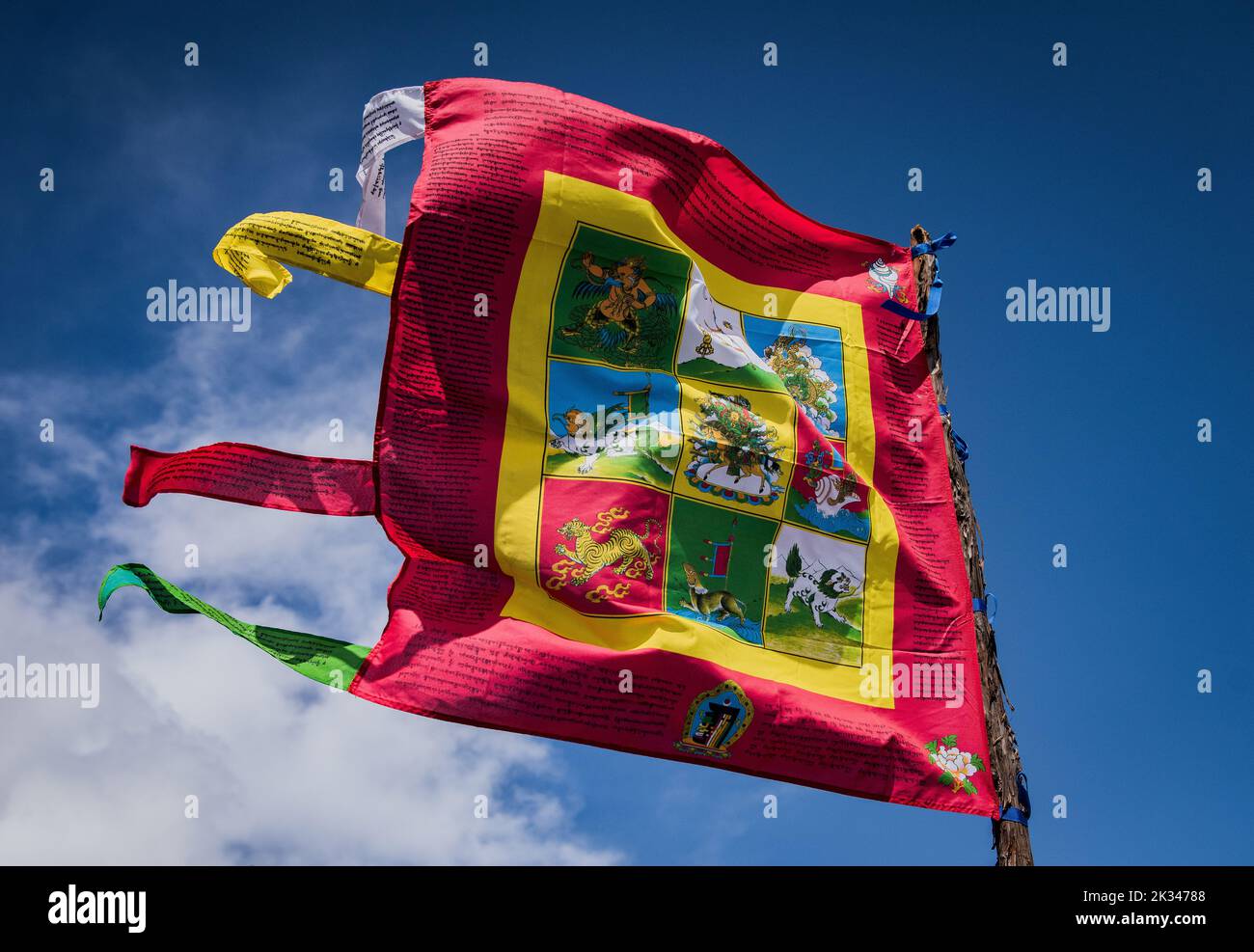 Gebetsfahne mit buddhistischen Symbolen auf einem Fahnenmast, der im Wind weht. Stockfoto