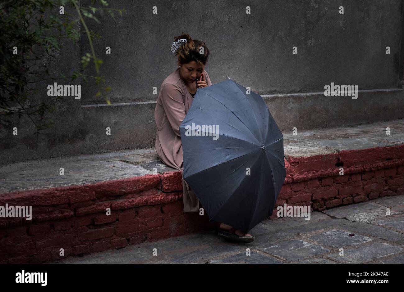 Eine Dame, die auf einer Wand mit einem offenen Schirm vor ihr sitzt. Stockfoto
