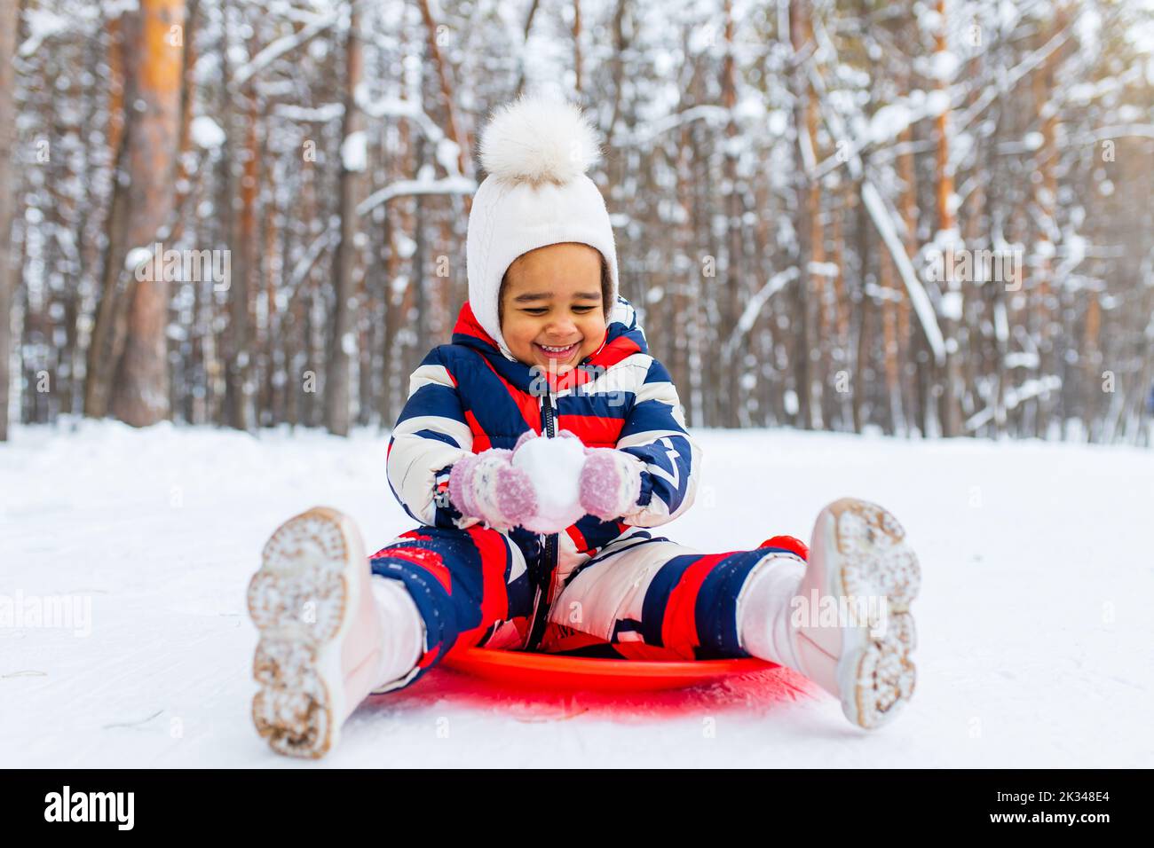 Kleines Mädchen spielt am verschneiten Wintertag im Park Schlittenfahrt den Hügel hinunter Stockfoto