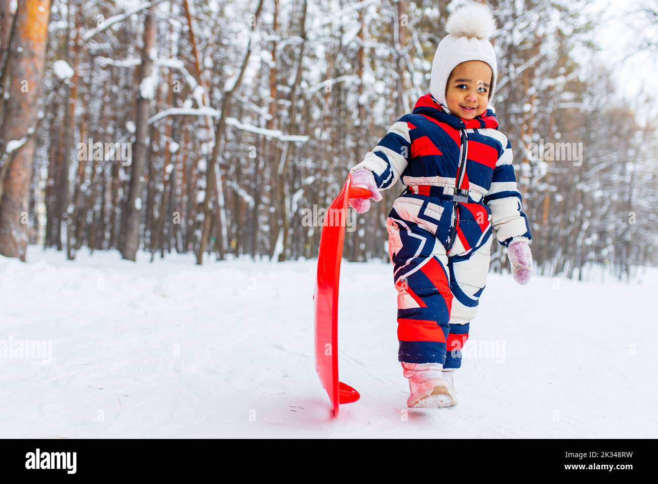 Kleines Mädchen spielt am verschneiten Wintertag im Park Schlittenfahrt den Hügel hinunter Stockfoto