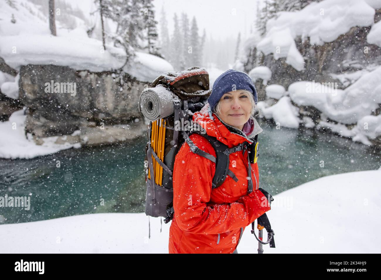 Portrait glückliche reife Frau beim Wandern mit Rucksack im Schnee entlang des Flusses Stockfoto