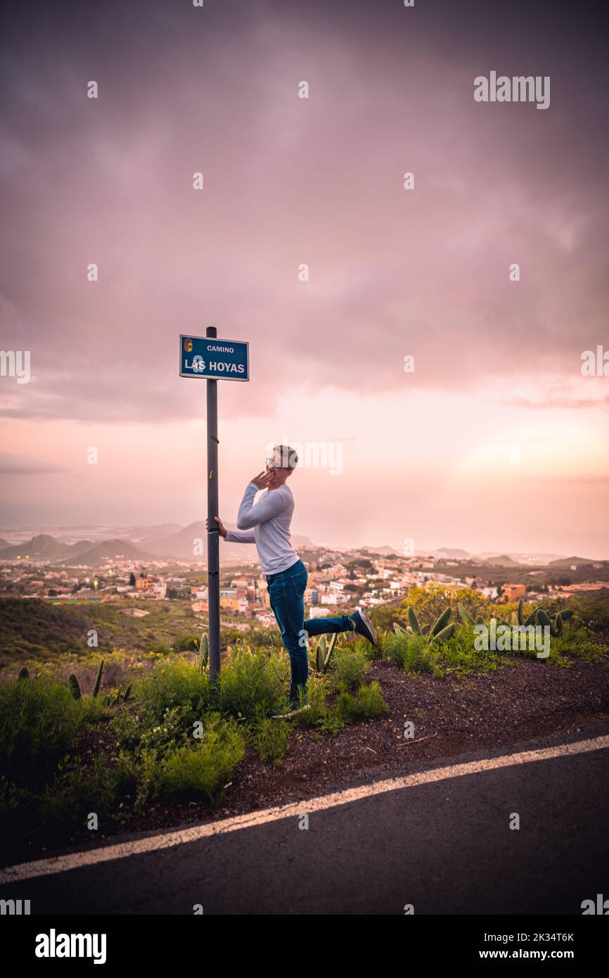 Ein vertikales Bild eines weißen Mannes, der sich neben dem Wegweiser auf der Camino Las Hoyas Road, Teneriffa, Spanien, posiert Stockfoto