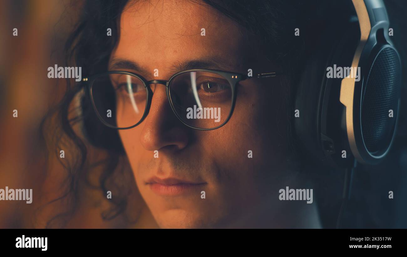 Kerl mit Kopfhörern und Brillen zu Hause, der in Freizeit am Computer im Internet surft und Musik hört oder aus der Ferne an Projekten arbeitet Stockfoto
