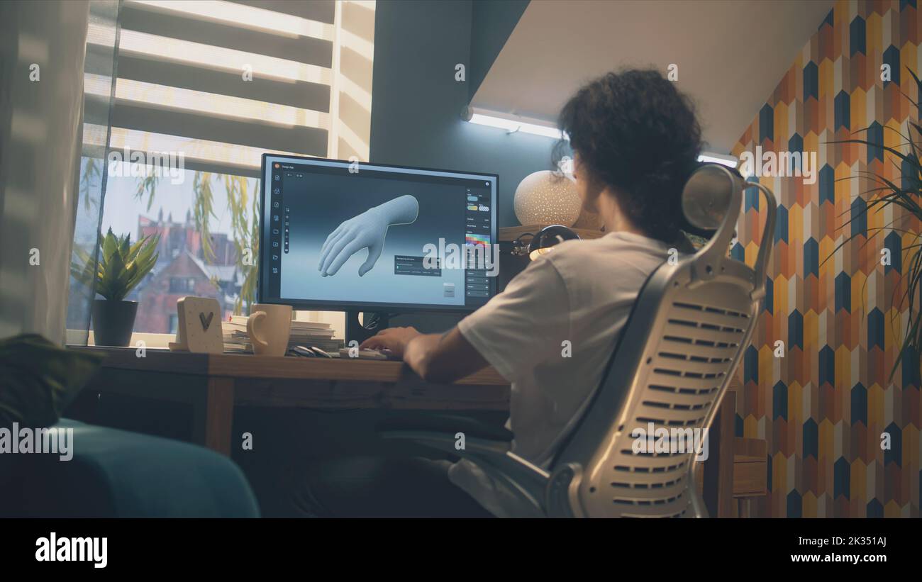 Männlicher Designer sitzt auf einem Stuhl am Tisch im Heimbüro und macht 3D Prototyp der menschlichen Hand im professionellen Programm für 3D, Modellierung mit pc. Stockfoto