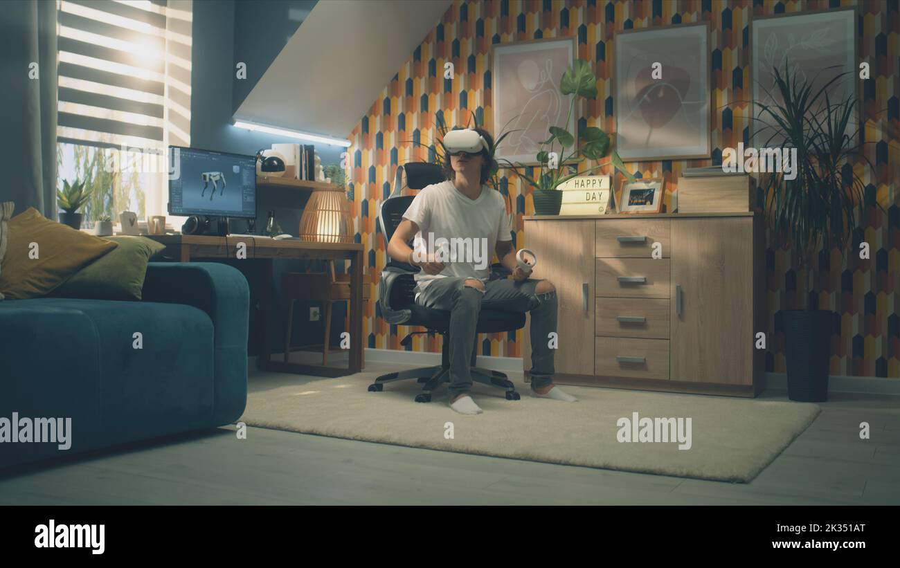 Mann, der in seiner Freizeit in seinem Zimmer Videospiele mit modernen VR-Headsets und drahtlosen Controllern spielt. Virtual-Reality-Gerät. Cyberspace und Metaverse Stockfoto
