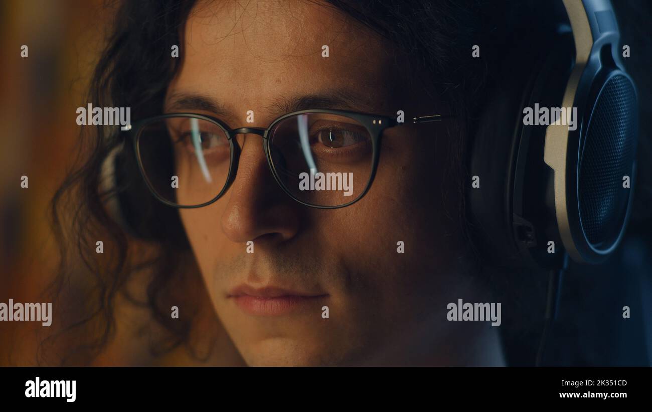 Kerl mit Kopfhörern und Brillen zu Hause, der in Freizeit am Computer im Internet surft und Musik hört oder aus der Ferne an Projekten arbeitet Stockfoto