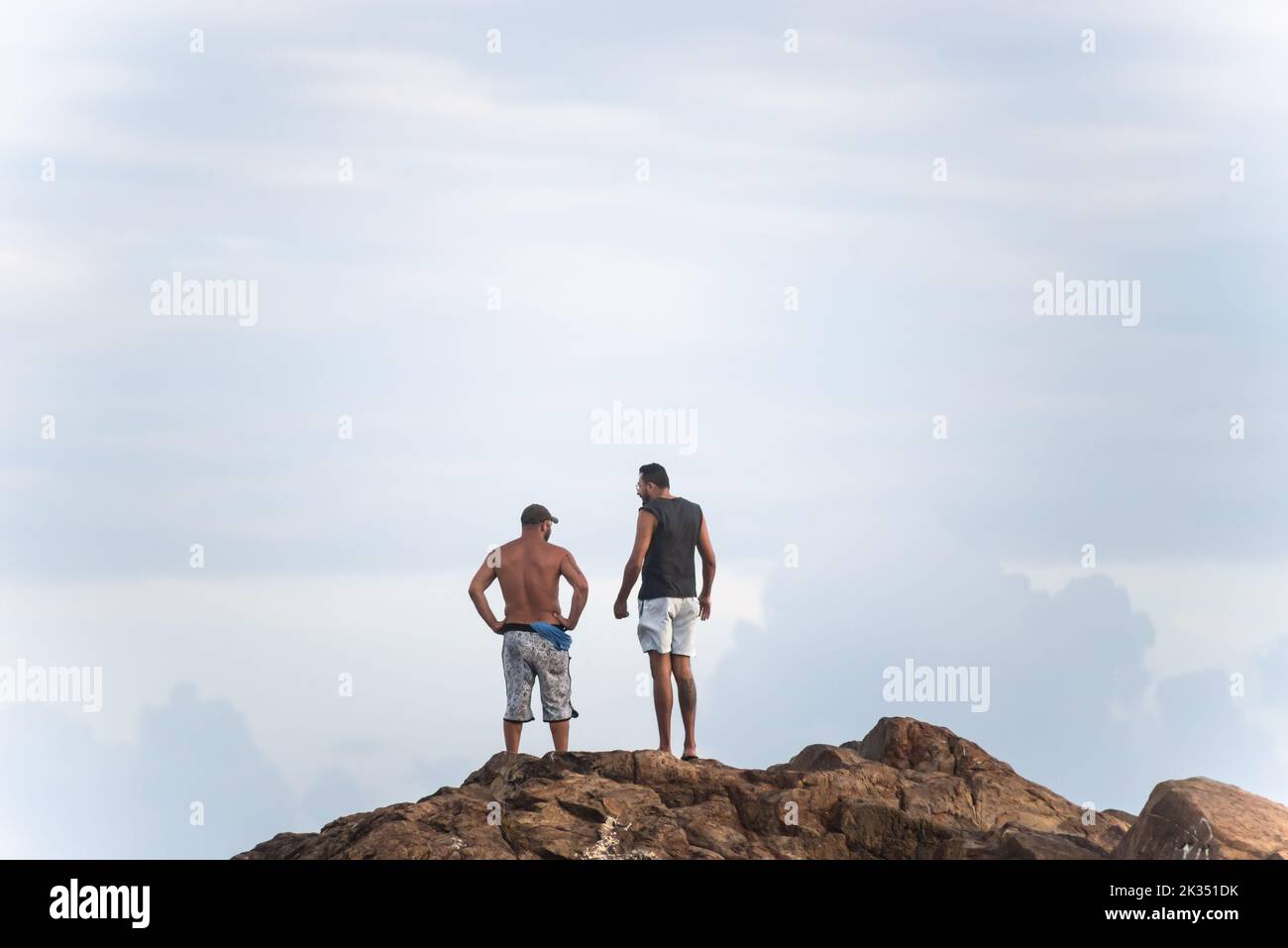 Die beiden Männer stehen auf einem großen Felsen am Farol da Barra Strand in Salvador, Bundesstaat Bahia, Brasilien Stockfoto