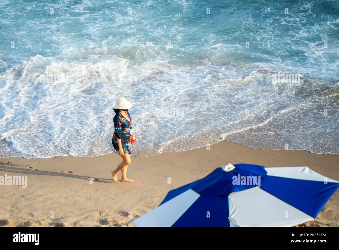 Eine Frau mit Hut wandert auf dem Sand von Farol da Barra Beach in Salvador, Bundesstaat Bahia, Brasilien Stockfoto
