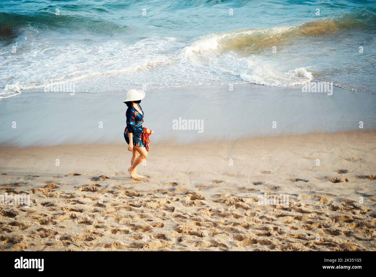 Eine Frau mit Hut wandert auf dem Sand von Farol da Barra Beach in Salvador, Bundesstaat Bahia, Brasilien Stockfoto