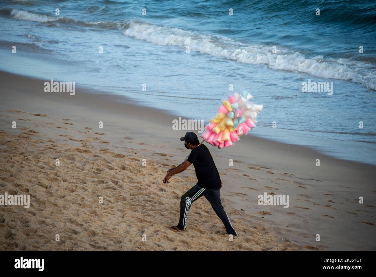Ein männlicher Verkäufer von Zuckerwatte, der auf dem Sand von Farol da Barra Beach in Salvador, Bahia, Brasilien läuft Stockfoto