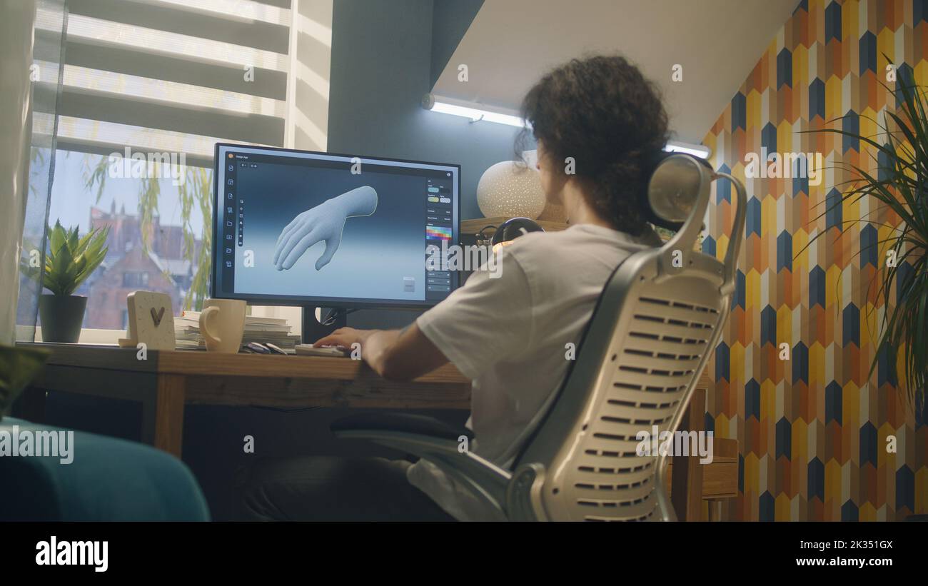 Männlicher Designer sitzt auf einem Stuhl am Tisch im Heimbüro und macht 3D Prototyp der menschlichen Hand im professionellen Programm für 3D, Modellierung mit pc. Stockfoto