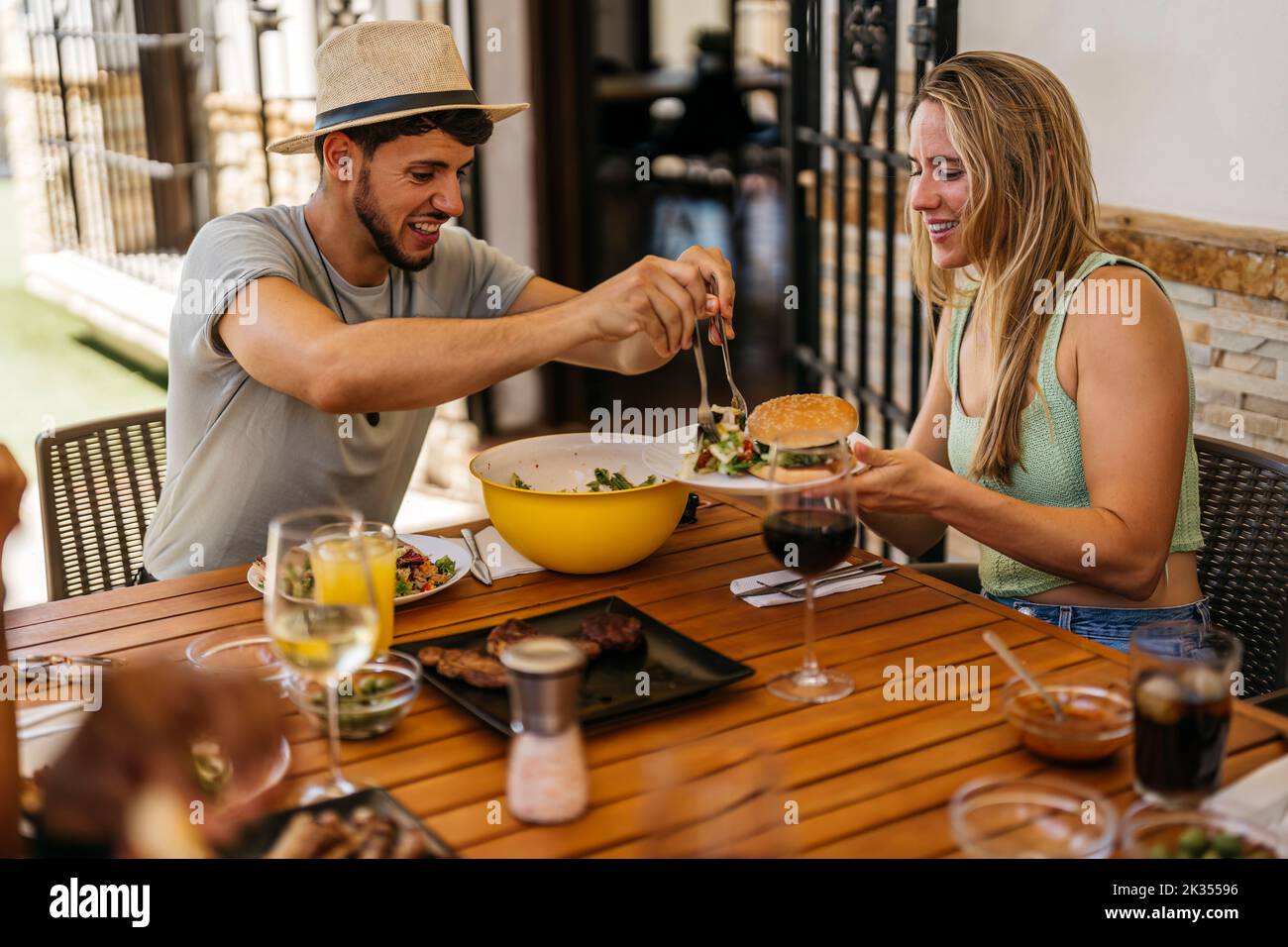 Der latino-Mann im Sombrero schmißt einer blonden kaukasischen Frau Salat als Hamburger Stockfoto