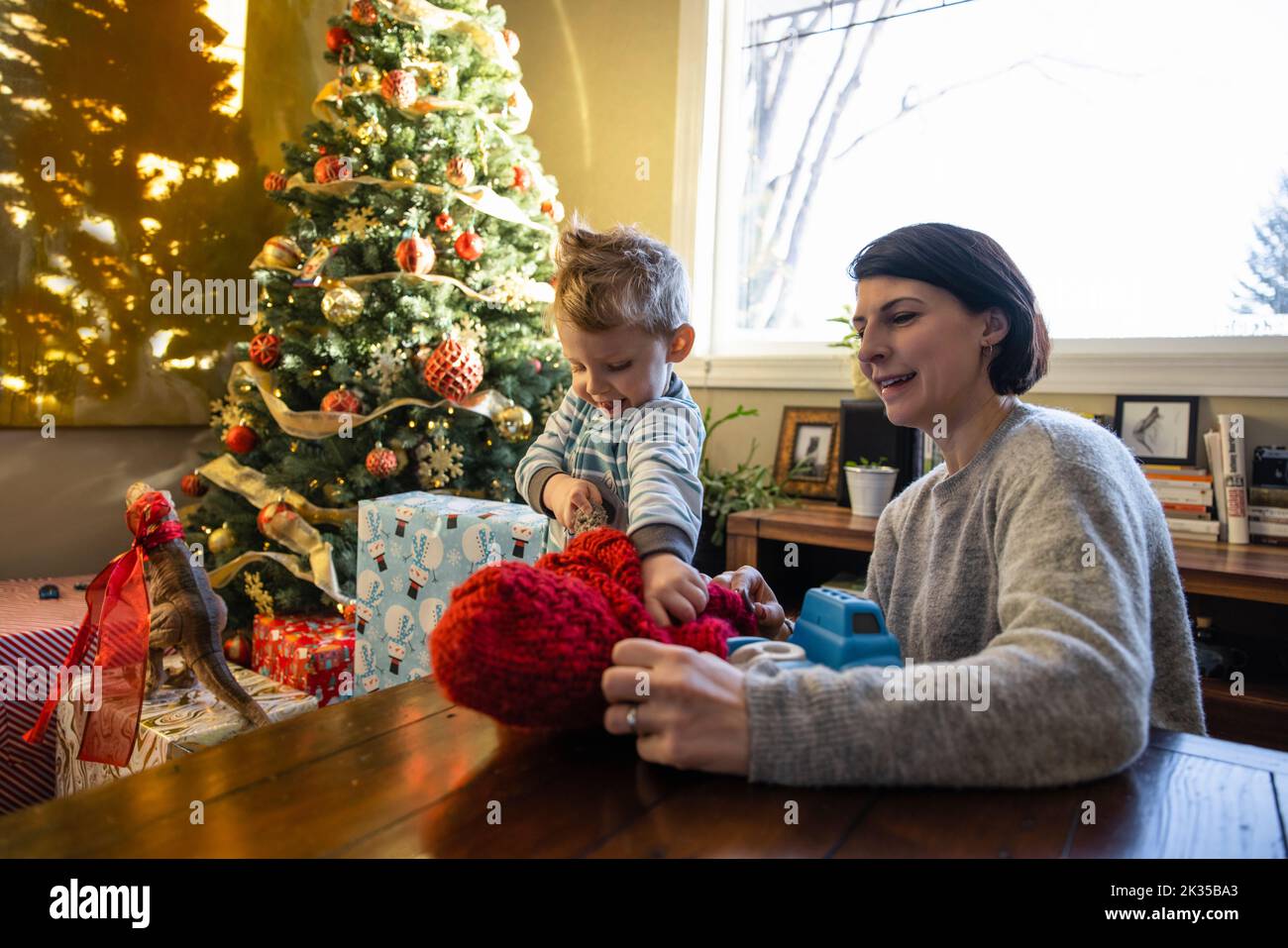 Mutter und Sohn spielen am Weihnachtsbaum im sonnigen Wohnzimmer Stockfoto
