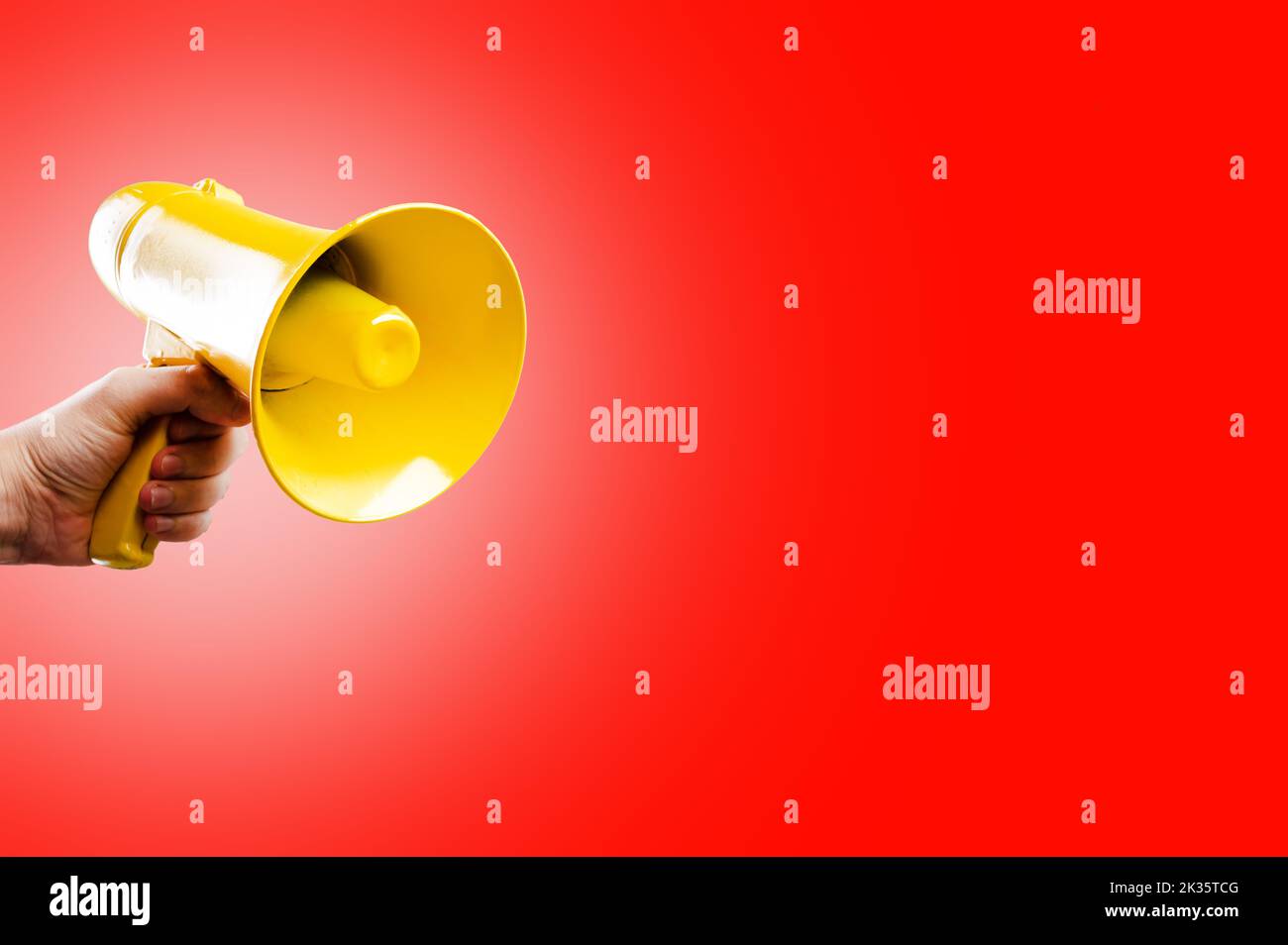 Auf einem leuchtend roten Hintergrund ein gelbes Megaphon in der Hand eines Mannes. Aktionen, Proteste, Demonstrationen, Kundgebungen, Wahldebatten. Presse, Fernsehen, Stockfoto