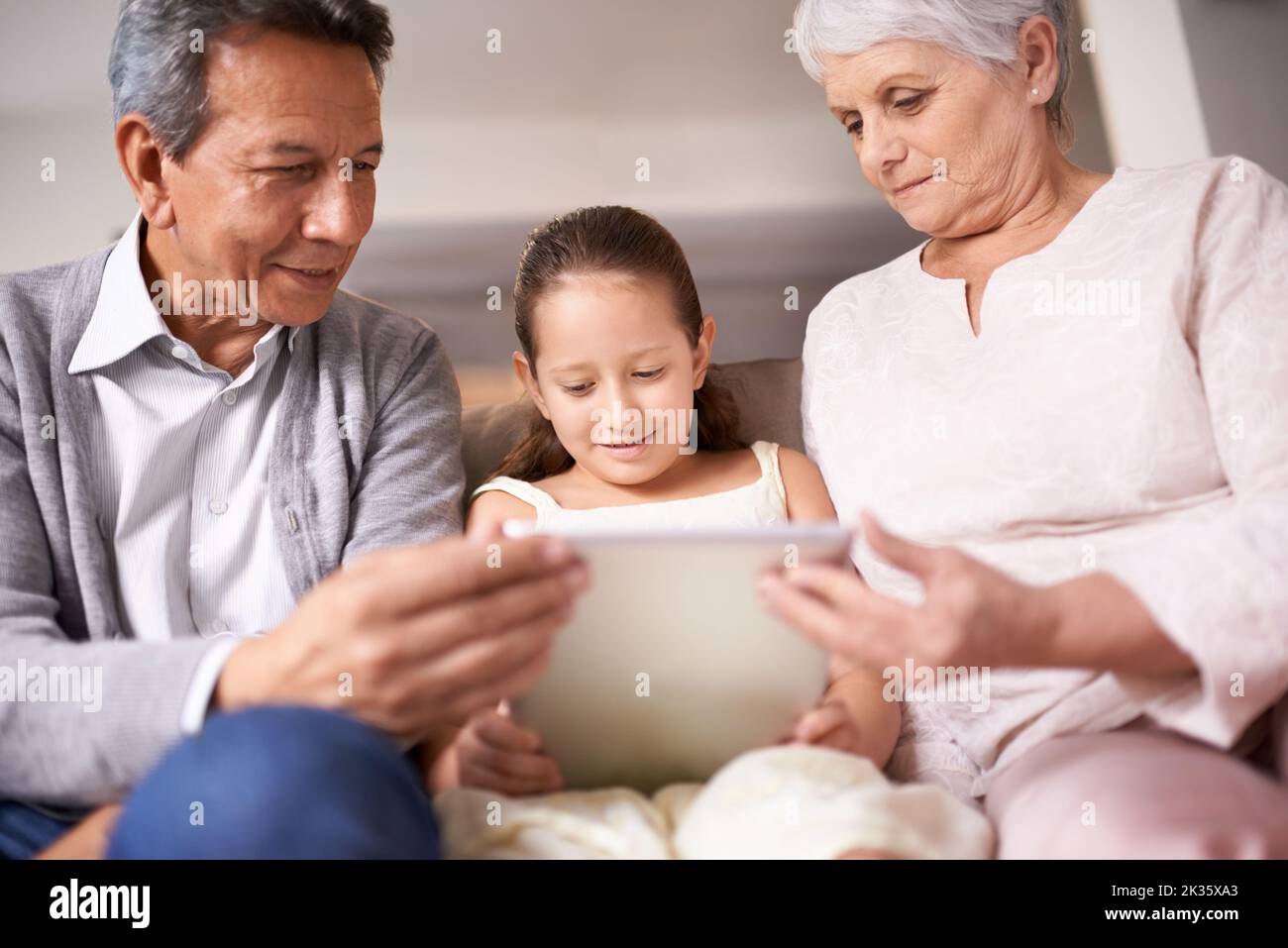 Tauschen von Lektionen aus dem Leben um Technologietipps. Ein kleines Mädchen, das ein Tablet benutzt, während es mit ihren Großeltern sitzt. Stockfoto