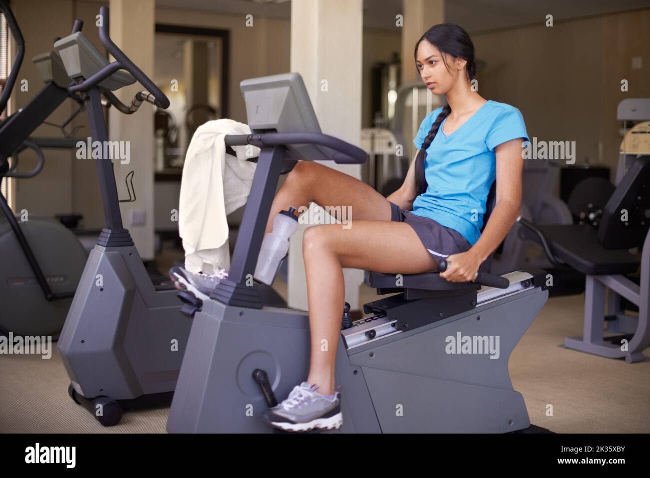 Die letzten Kilometer. Eine junge ethnische Frau, die auf einem stationären Fahrrad in der Turnhalle trainieren. Stockfoto