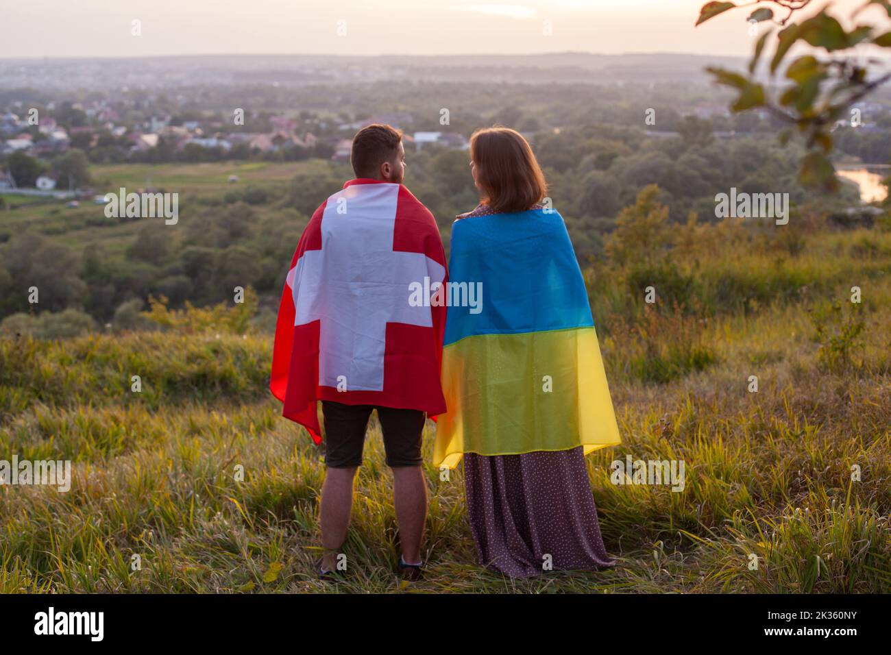 Paar bedeckt in Ukraine und Schweiz Flaggen. Konzept der Freundschaft zwischen der Ukraine und der Schweizerischen Eidgenossenschaft. Liebe zwischen zwei Ländern. Man und wo Stockfoto