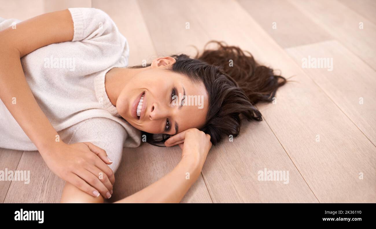 Flirts auf dem Boden. Eine junge Frau lächelt der Kamera zu, während sie auf dem Boden liegt. Stockfoto