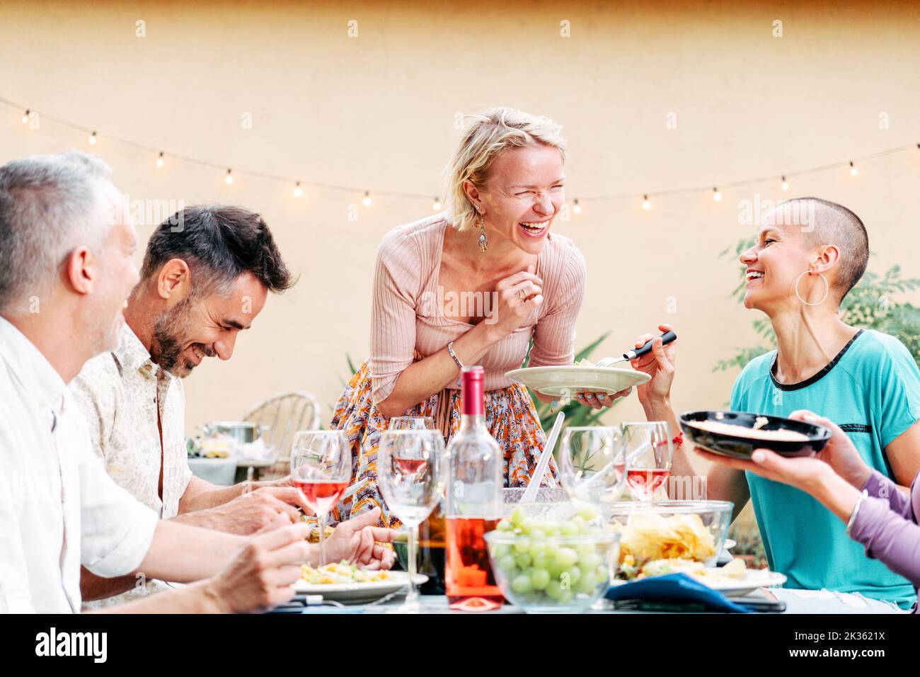 Reife Menschen feiern eine grillparty und teilen sein Essen mit seinen Freunden. Hübsche Frau bringt einen Salat auf den Tisch. Lifestyle-Konzept. Stockfoto