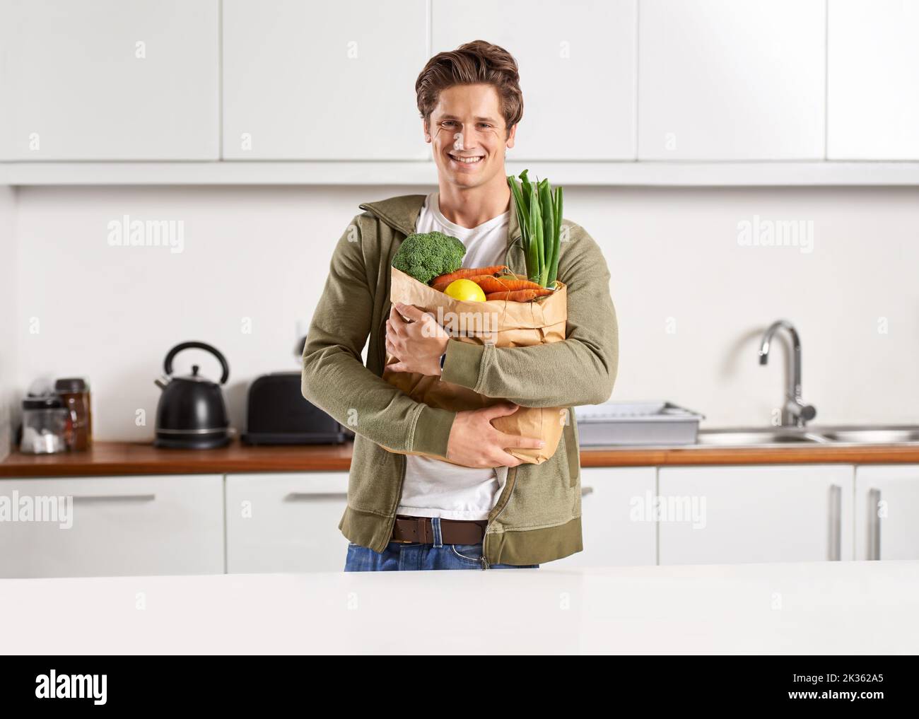 Frisch vom Markt. Ein junger Mann in einer Küche, der einen braunen Papierbeutel mit Gemüse hält. Stockfoto