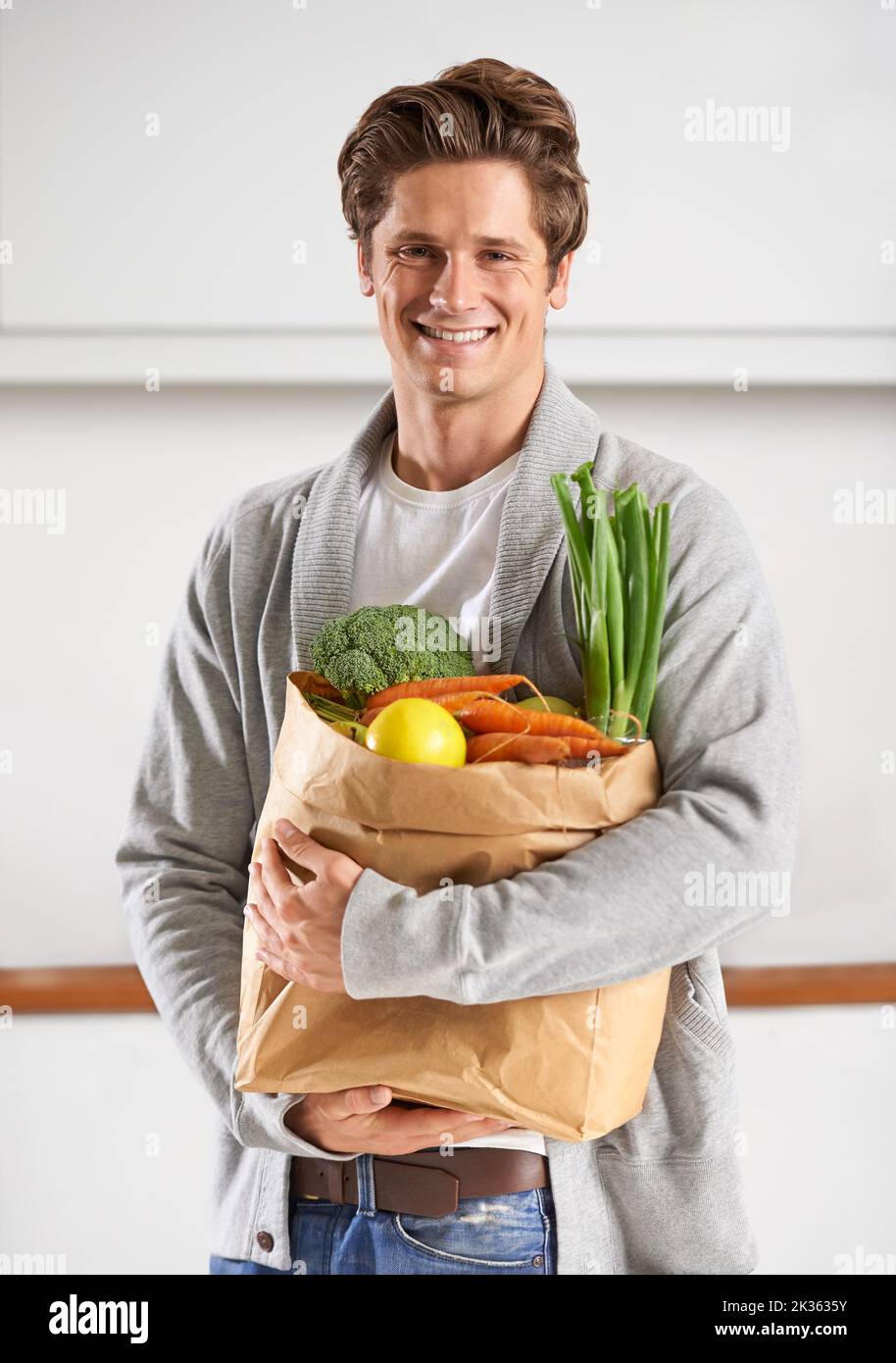 Nur Bio für mich. Ein junger Mann in einer Küche, der einen braunen Papierbeutel mit Gemüse hält. Stockfoto