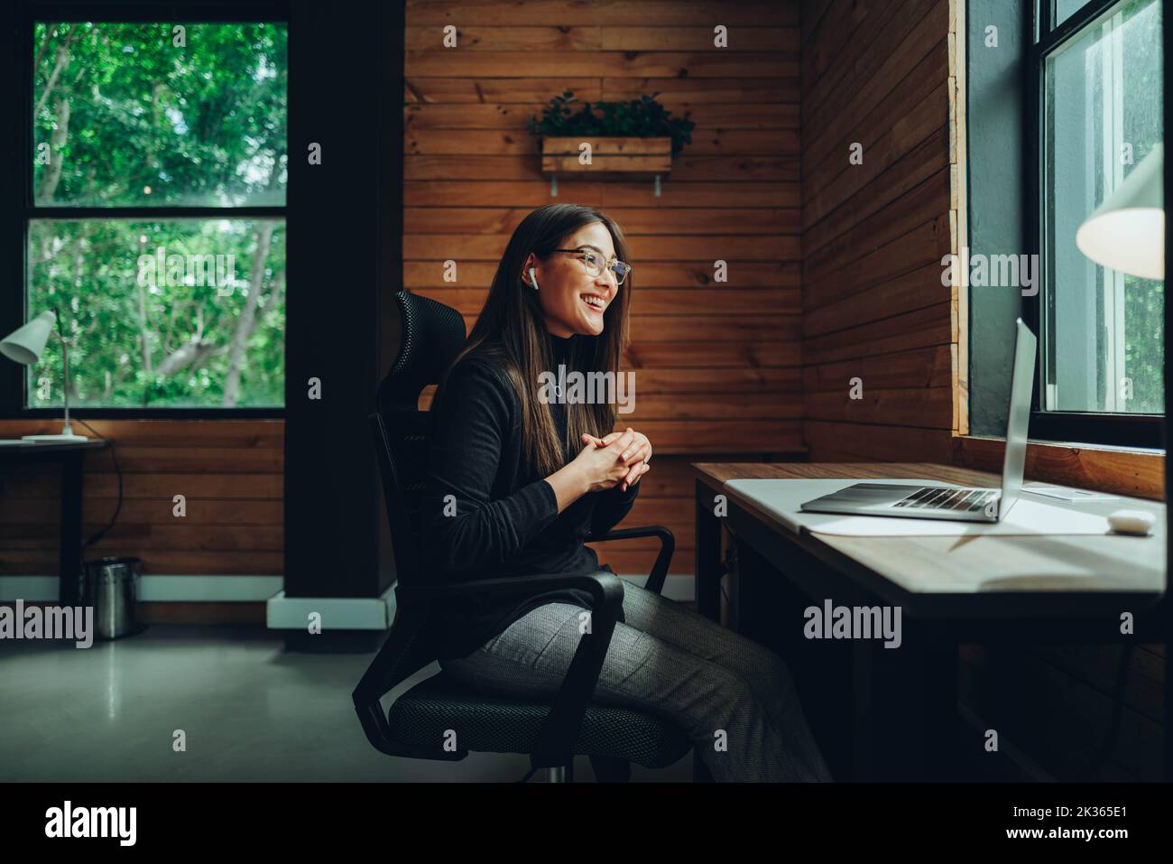 Fröhliche junge Geschäftsfrau mit einem Videoanruf in einem modernen Co-Working-Raum. Glückliche Unternehmerin, die mit ihren Geschäftspartnern kommuniziert Stockfoto