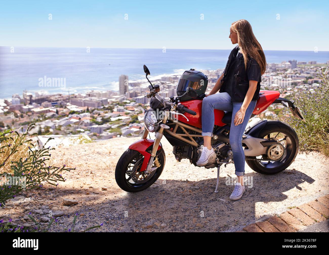 Weg vom Chaos des Lebens. Eine schöne junge Frau, die auf ihrem roten Motorrad sitzt. Stockfoto