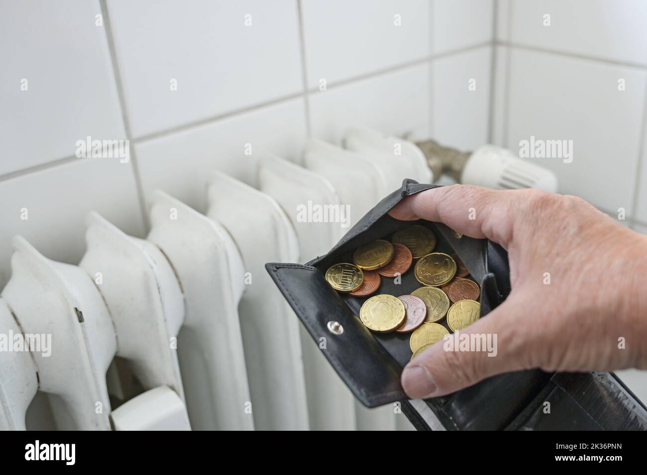 Hand öffnet eine Brieftasche mit wenigen Münzen vor einem alten, ineffizienten Heizgerät in einer Mietwohnung, Energiekrisen erhöhen den Preis für Gas und Stockfoto