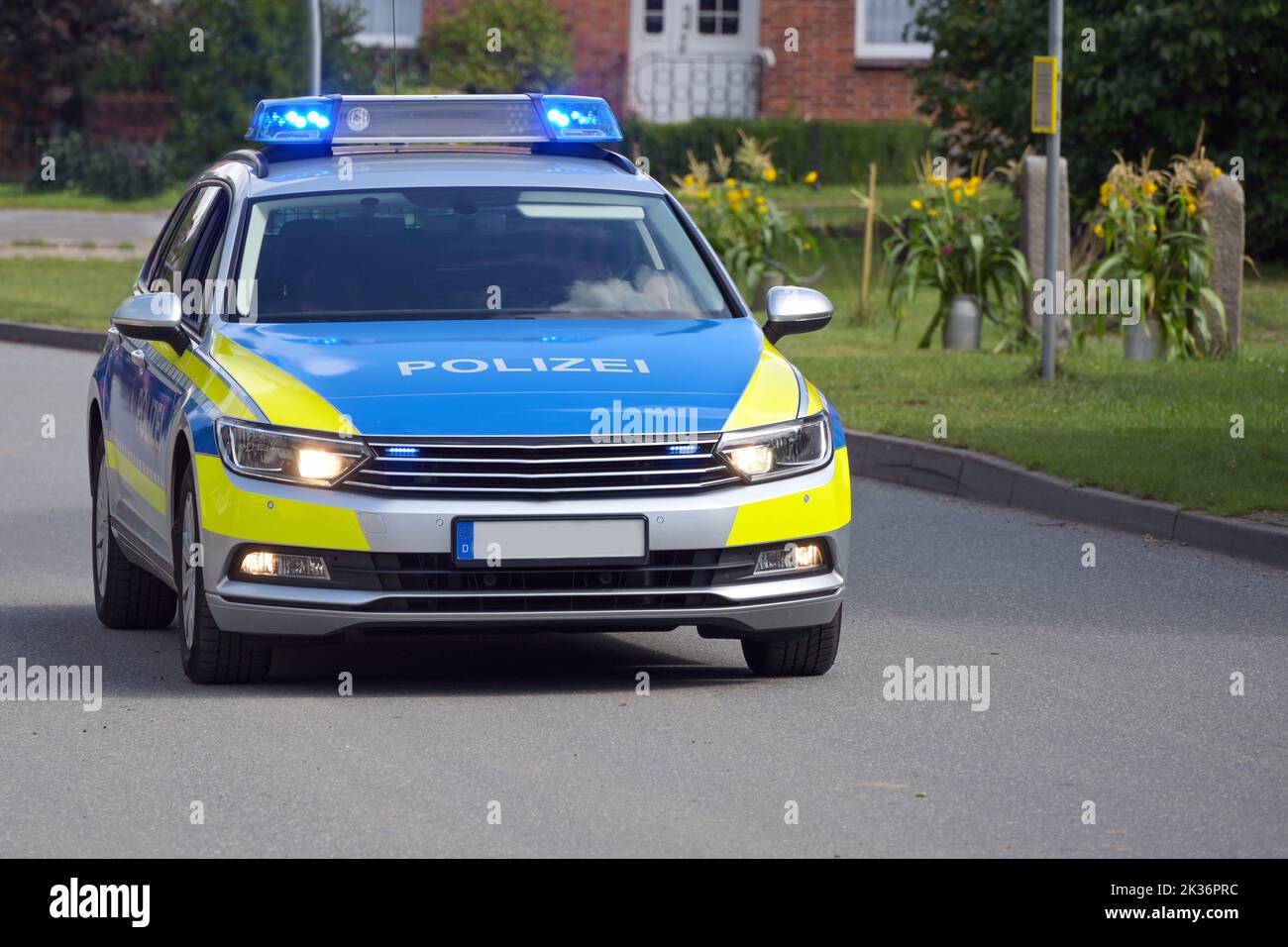 Deutscher Polizeiwagen im Einsatz, der mit blinkenden blauen Lichtern durch einen ländlichen Vorort fährt, Inschrift Polizei bedeutet Polizei, Kopierraum, ausgewählter Fokus Stockfoto