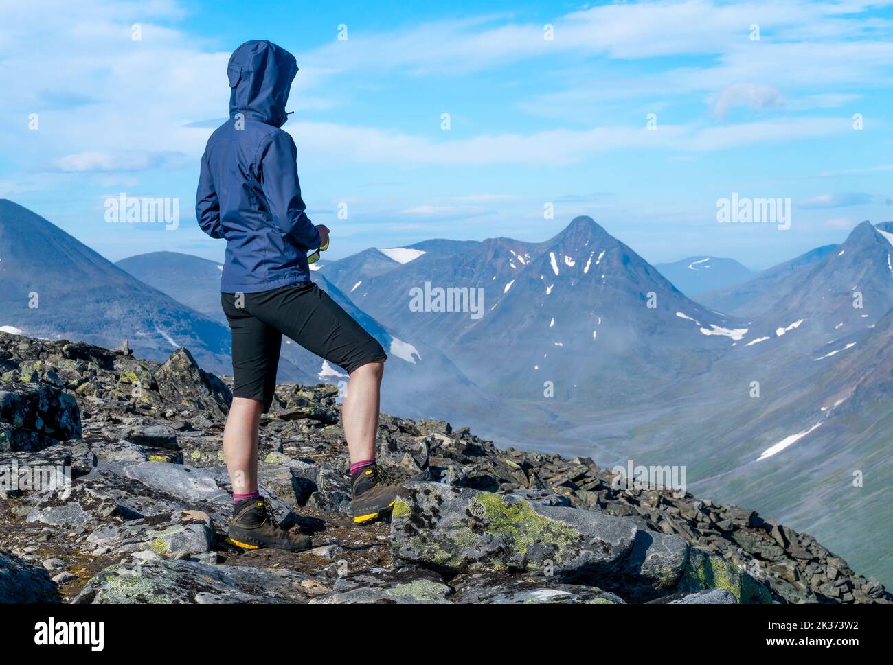 Weibliche Wanderin in blauer Jacke mit Blick auf die riesige arktische Berglandschaft vom Gipfel des Berges. Top of Naite, Sarek National Park, Schweden. Wandern Stockfoto