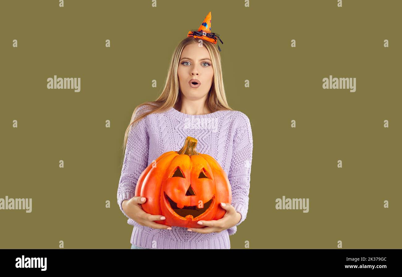 Frau mit lustig überrascht Ausdruck hält schweren halloween Kürbis auf khaki Hintergrund im Studio Stockfoto