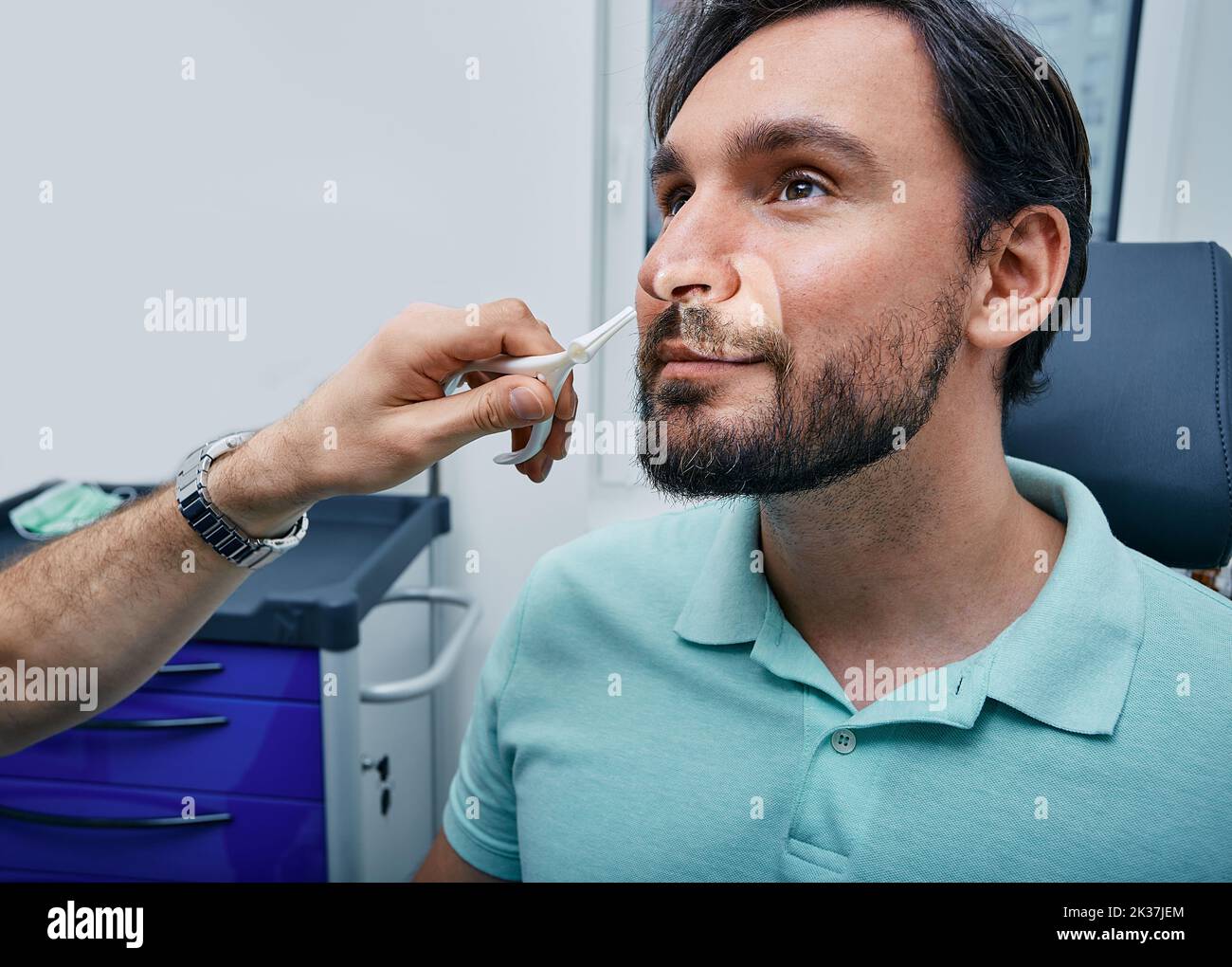 Erwachsener Mann während der Rhinoskopie in der HNO-Praxis. Arzt mit Nasenspekulum oder Rhinoskop zur Untersuchung des Nasenbereichs des Patienten Stockfoto