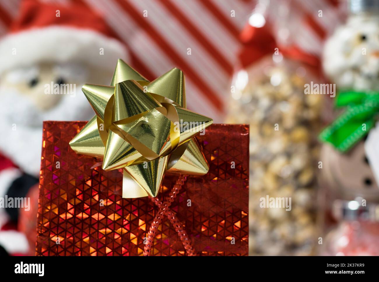 Verschiedene Weihnachtsdekorationen und Geschenke mit Fokus auf Geschenktasche und Schleife im Vordergrund, Hintergrund aus buntem Geschenkpapier. Stockfoto