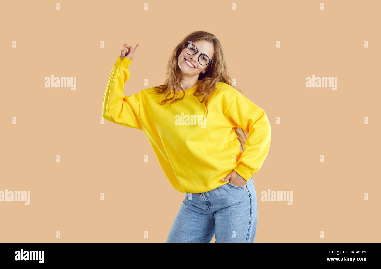Happy schöne Student Mädchen in gelben Sweatshirt und Brille posiert auf beigem Hintergrund Stockfoto