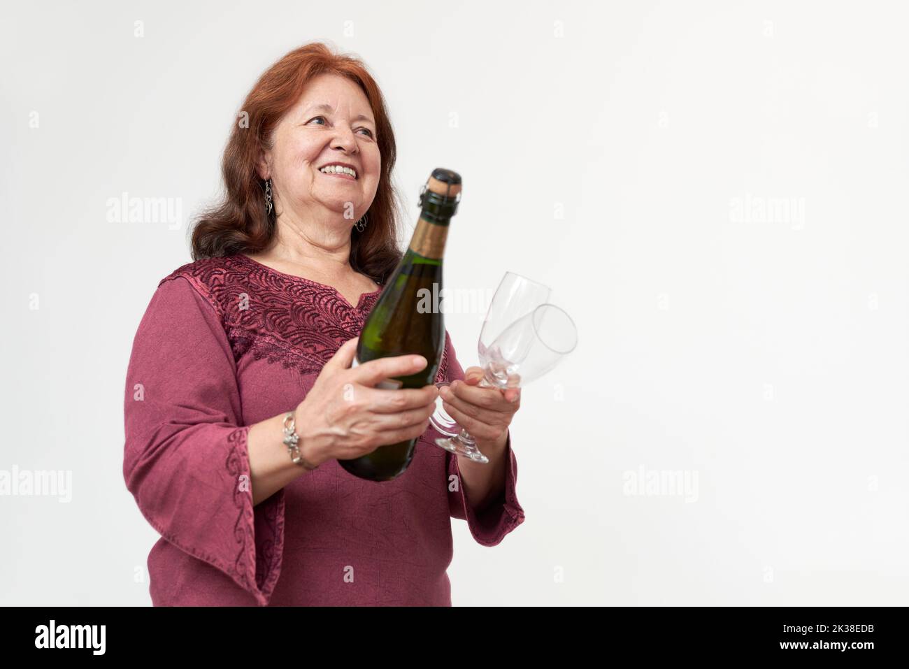 Die hispanische reife Frau lächelt, während sie eine Flasche Champagner oder Apfelwein und ein paar Gläser in der Hand hält. Konzept des feierlichen Toasts. Komposition mit Kopie Stockfoto