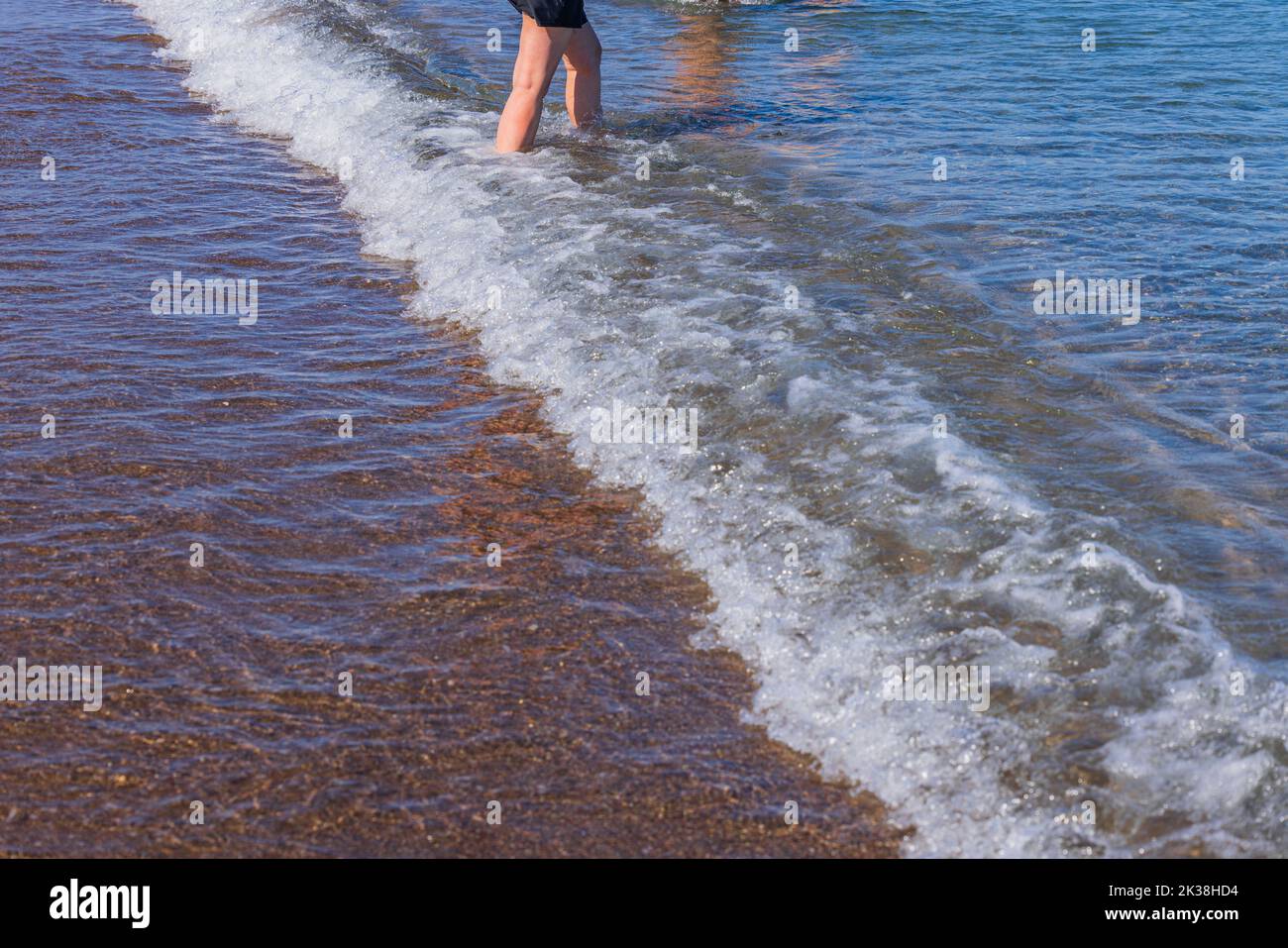 Blick auf die Beine einer Frau, die vom Ufer des Sandstrandes ins Meer eindringt. Griechenland. Stockfoto