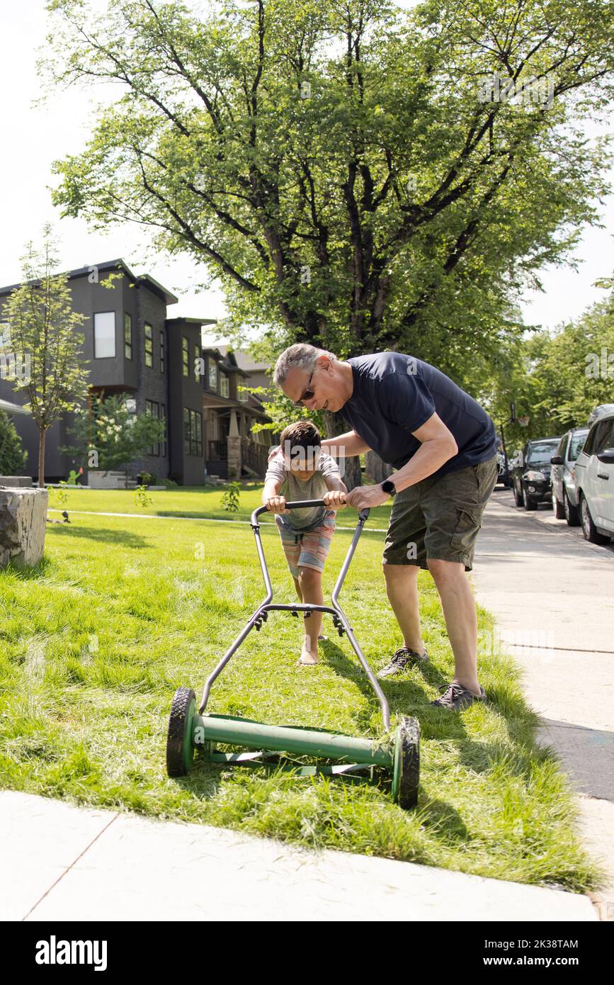 Großvater lehrt Enkel, wie man Rasen im sonnigen Vorgarten mäht Stockfoto