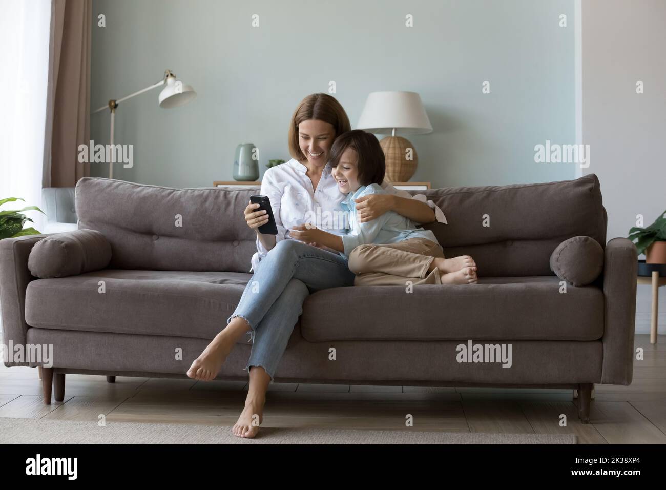 Millennial Mutter umarmt kleinen Sohn auf der Couch, mit Online-App Stockfoto