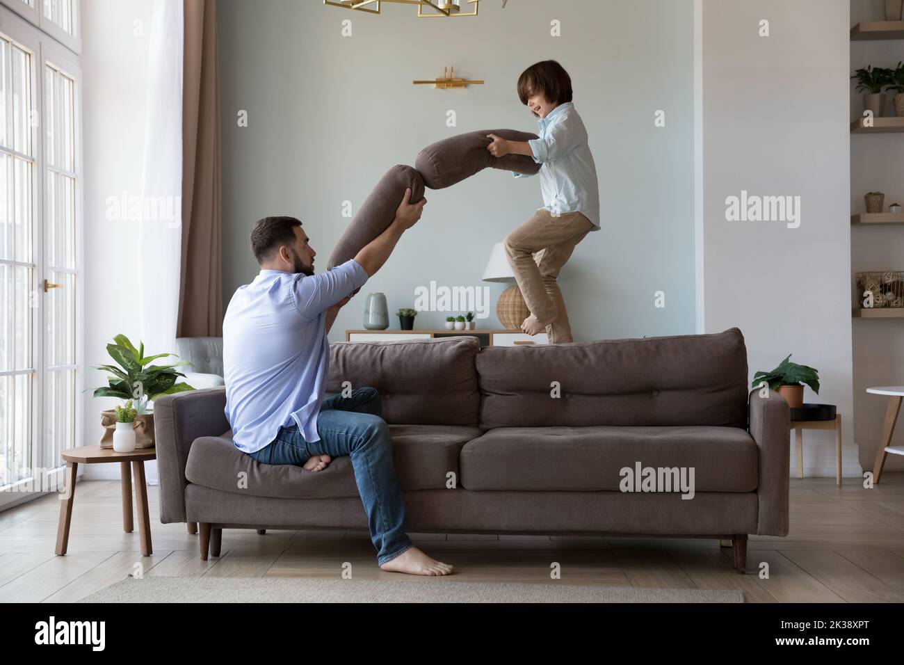 Aufgeregter Sohn und Vater kämpfen mit Kissen auf dem Sofa Stockfoto