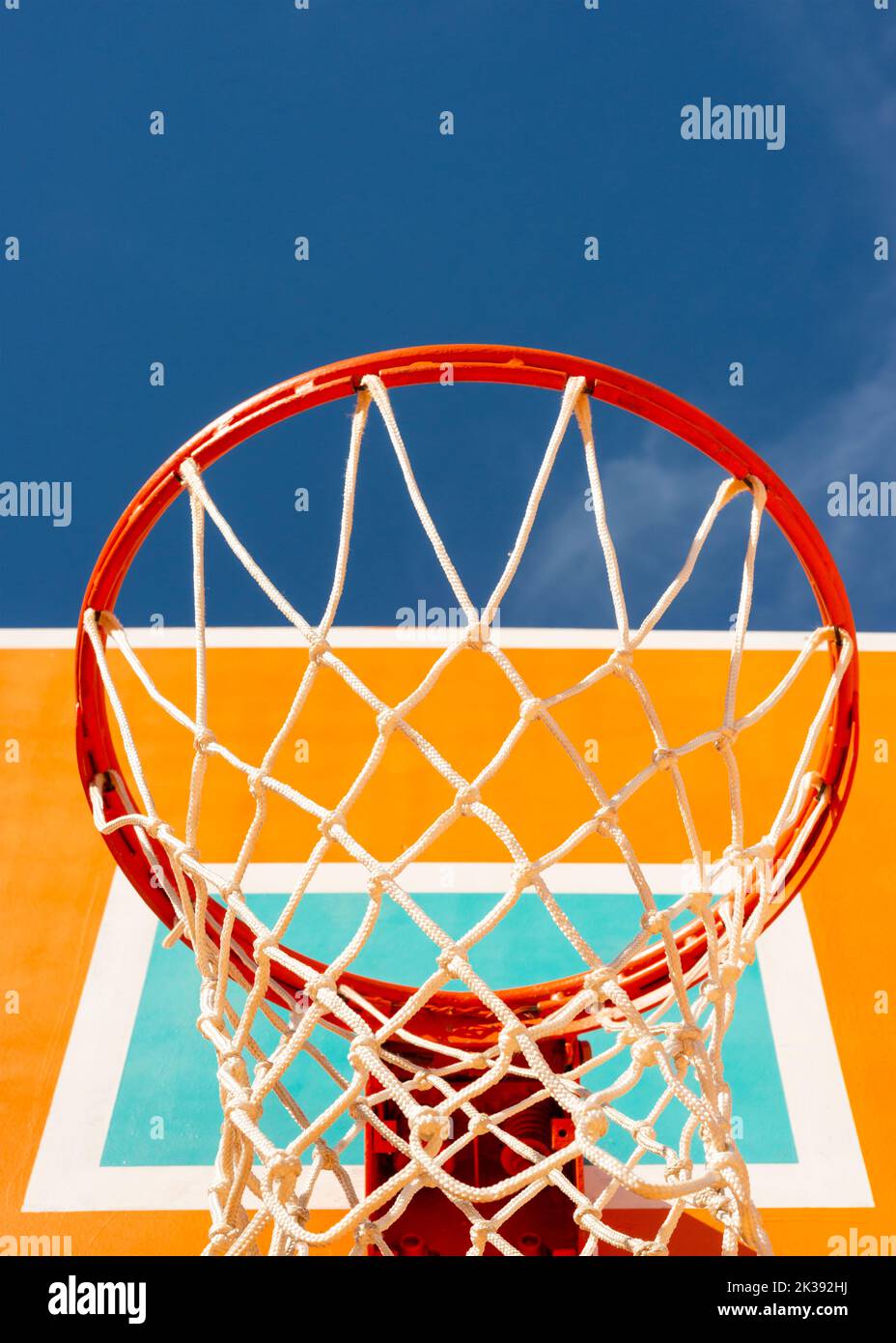 Farbenfrohe orangefarbene Basketballrückwand mit rotem Reifen und einem Netz gegen blauen Himmel mit Blick auf den niedrigen Winkel mit Kopierbereich Stockfoto