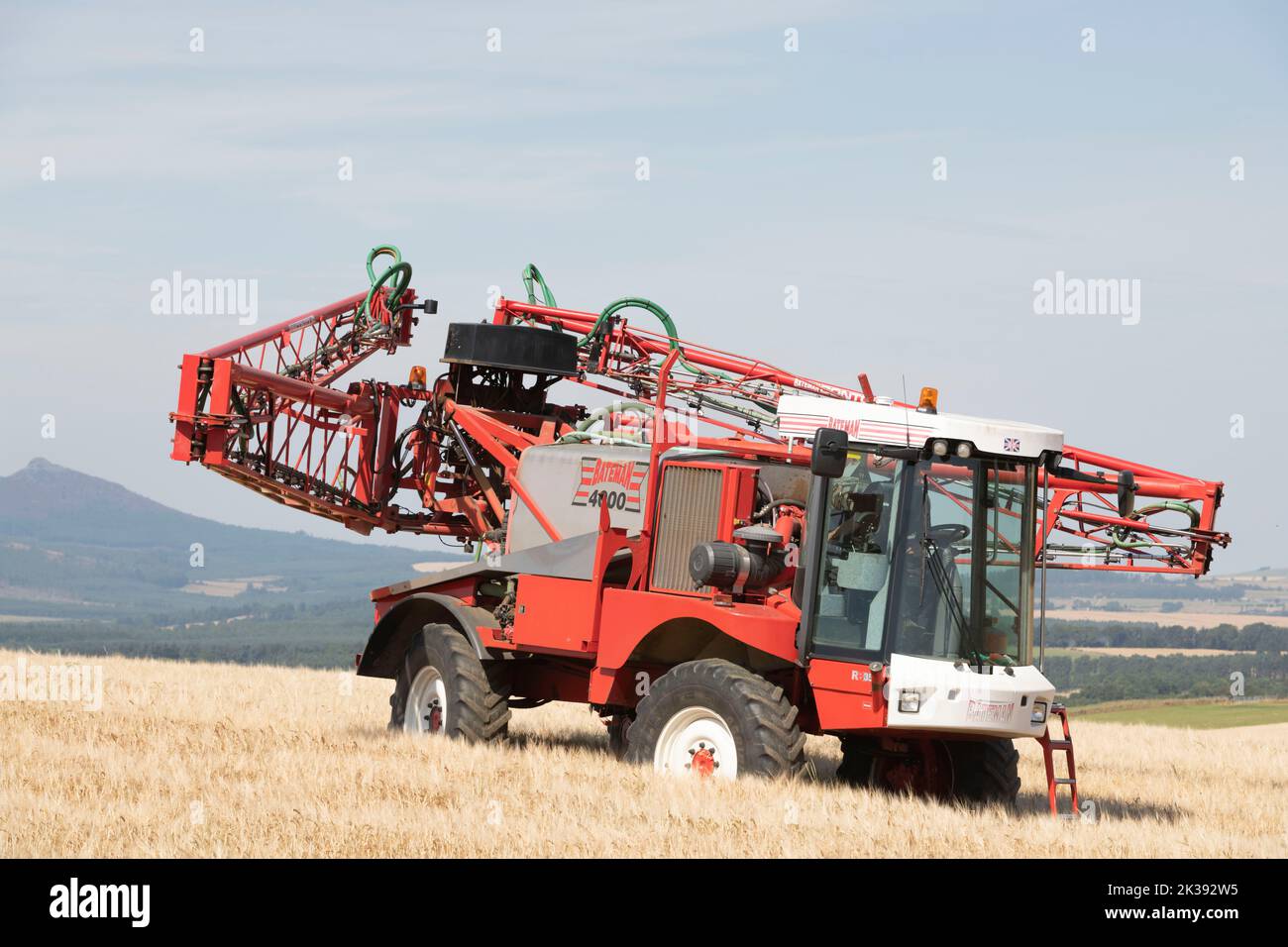 Ein selbstfahrender Bateman 4000 Crop Sprayer in einem Feld von Gerste, der seinen Sprühboom faltet, mit Bennachie, Aberdeenshire, im Hintergrund Stockfoto