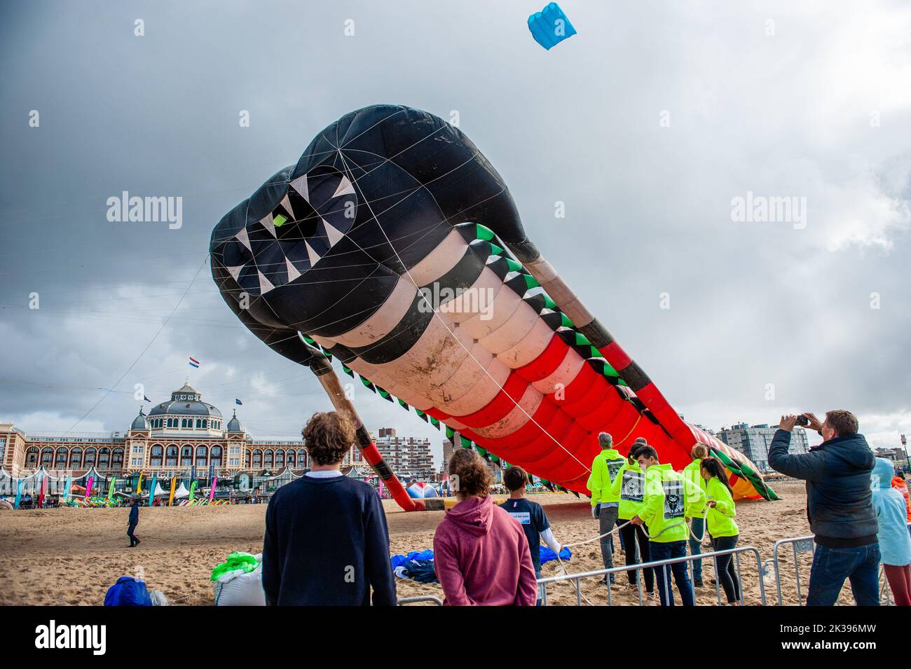 Die Menschen werden gesehen, wie der große Drachen in den Himmel zu starten versucht. Das International Kite Festival Scheveningen macht das Beste aus den konstant vorherrschenden Winden, die entlang des Strandresorts von Den Haag wehen. Drachenbauer und Enthusiasten aus der ganzen Welt kommen zusammen, um die Früchte ihrer kreativen Arbeit zu fliegen. Fast am Ende der Veranstaltung flog das Holland Kite Team ihren großen Drachen, der 1997 offiziell den Guinness-Weltrekord beim Bristol International Kite Festival erhielt. Bei der jährlichen Veranstaltung wird der Himmel über dem südlichen Teil des Strandes von Scheveningen mit riesigen Drachen übersät Stockfoto